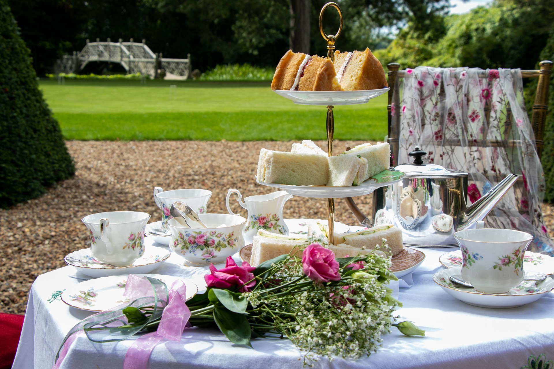 Set table for traditional vintage british afternoon tea with cake, sandwiches and view of garden